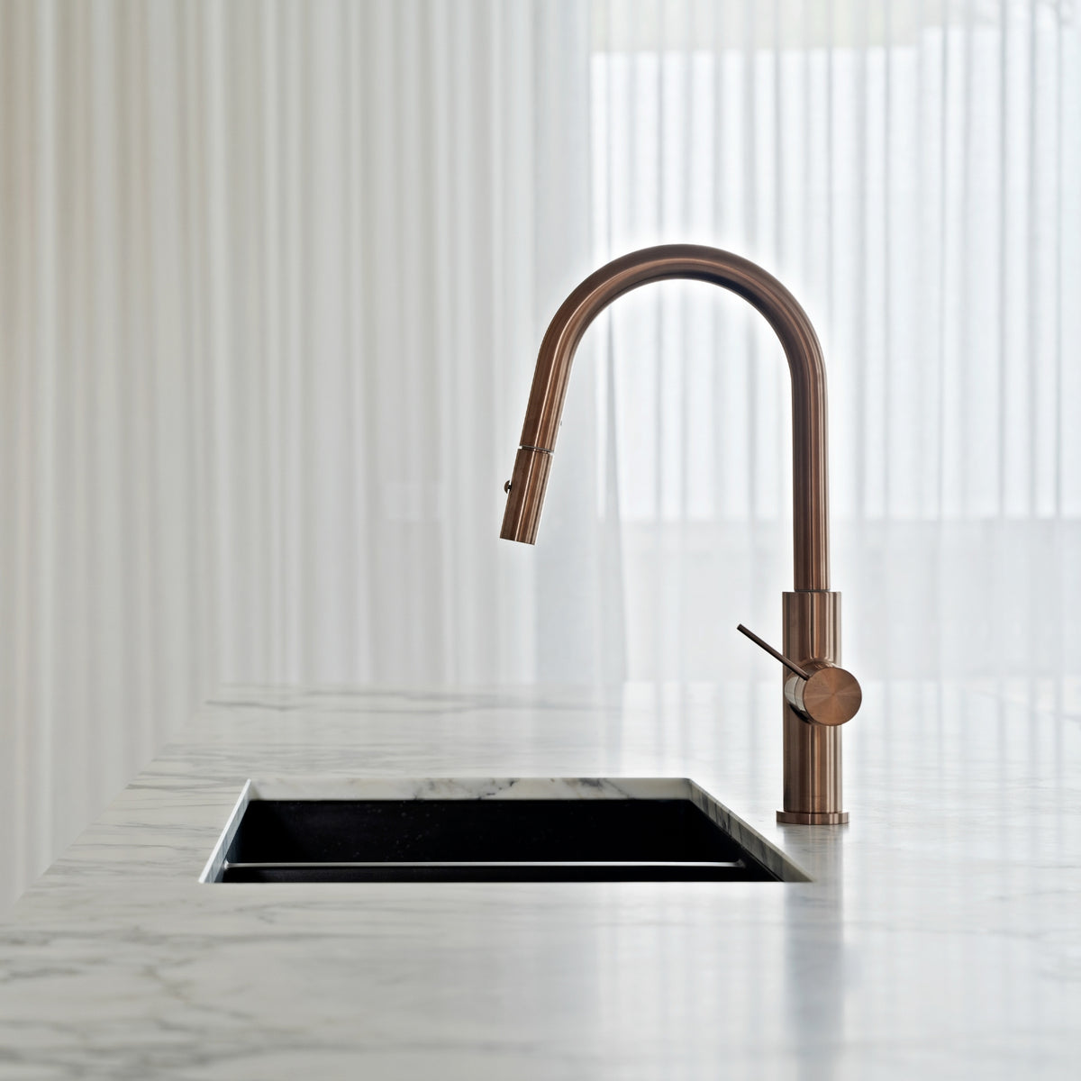 Nero Mecca brushed bronze pull out kitchen mixer with arched spout and single lever on a marble benchtop above a black sink
