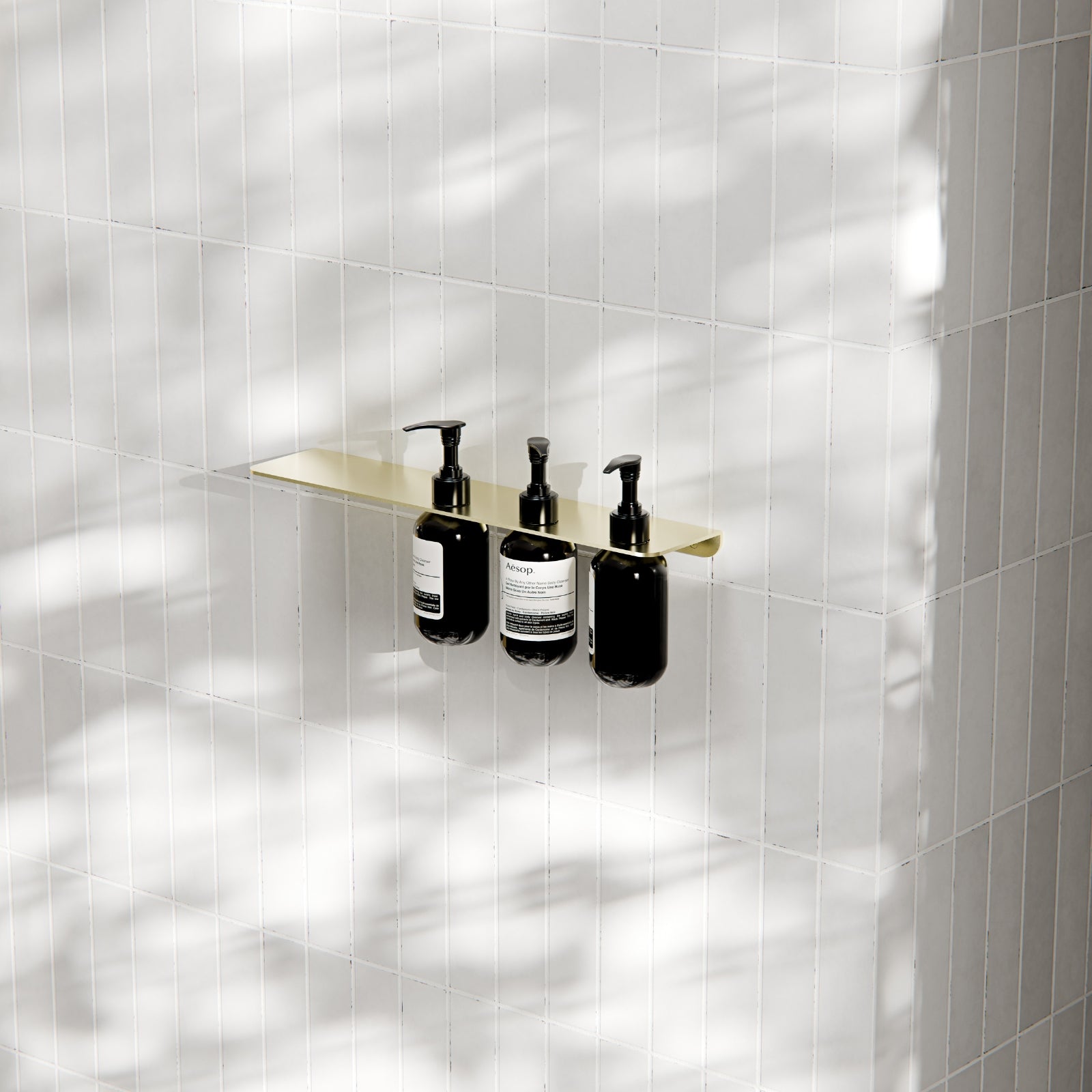 Nero Mecca triple soap bottle holder with shelf in brushed gold, wall-mounted on white tiled bathroom wall with three pump bottles
