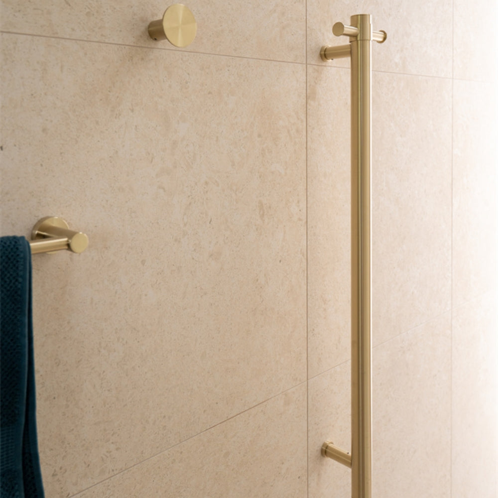 Nero vertical towel rail in brushed gold on a tiled bathroom wall, shown with matching hooks and towel rail hardware.