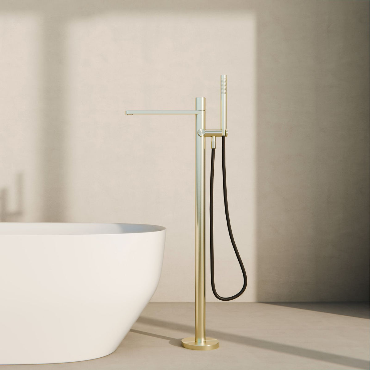 Nero Pure freestanding bath mixer in brushed gold beside a white bath, with floor-mounted shower hose and hand shower