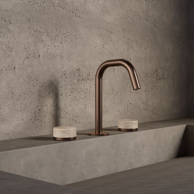 Nero Serenity three-piece basin set in brushed bronze with travertine handles, shown in a modern concrete bathroom setting
