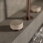 Close-up of Nero Serenity basin set in brushed bronze, showing the Rome travertine handle and edge spout on a grey vanity base