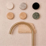 Nero Serenity brushed gold arc spout with Carrara marble handle samples on textured wall, top view