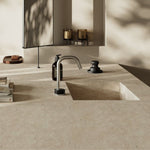 Brushed gold Nero Serenity arc spout tap on a stone-look vanity with black handle in a bathroom setting