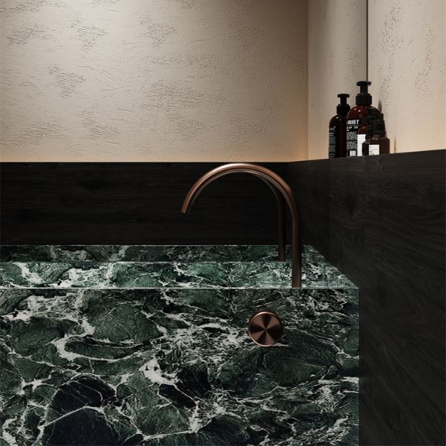 Nero Serenity progressive mixer with arc spout and metal handle in brushed bronze, over a green marble basin view