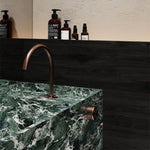 Nero Serenity brushed bronze progressive mixer tap with arc spout, installed on a green stone basin in bathroom setting