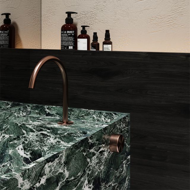 Nero Serenity brushed bronze progressive mixer tap with arc spout, installed on a green stone basin in bathroom setting