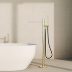 Nero Pure freestanding bath mixer in brushed gold, floor-mounted beside a white oval bath with hand shower and hose