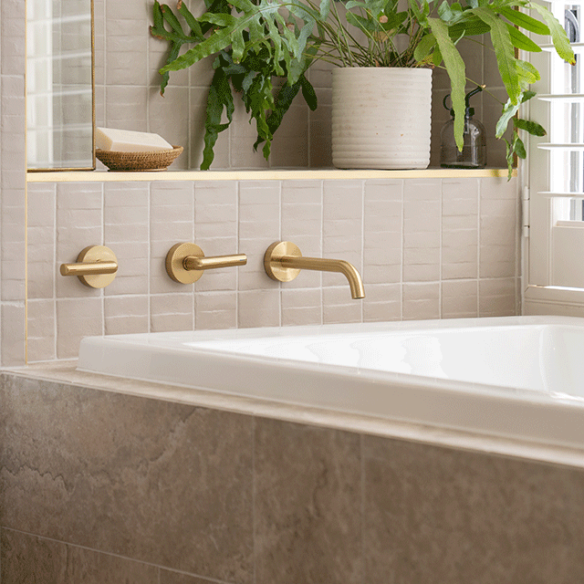 Caroma Newbury white rectangular island bath inset in a tiled hob, with brass wall mixer and warm bathroom setting