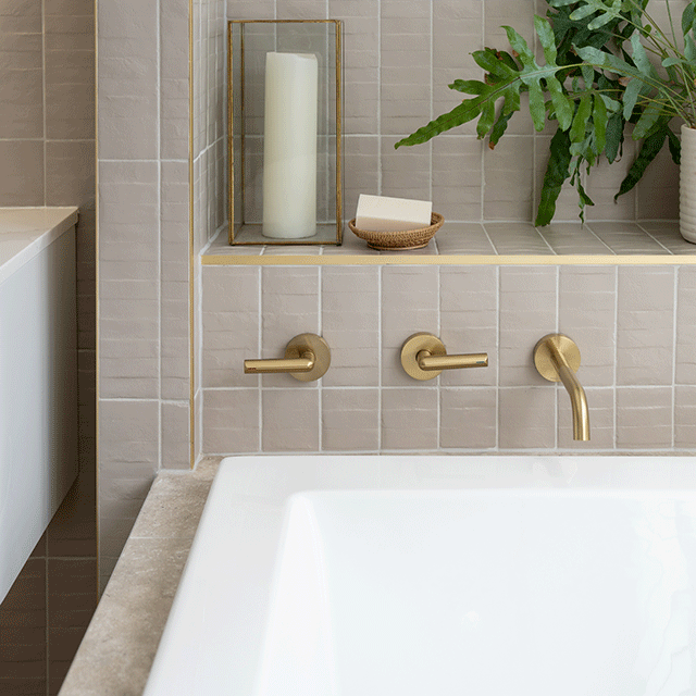 Caroma Newbury island bath in white acrylic, inset in tiled hob with brushed brass taps and shelf styling