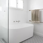 Phoenix Cromford brushed nickel wall-mounted basin/bath tap set over a white bath in a bright bathroom