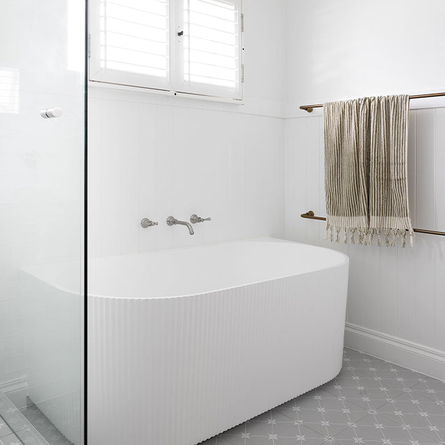 Phoenix Cromford brushed nickel wall-mounted basin/bath tap set over a white bath in a bright bathroom