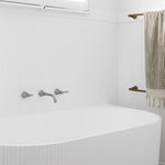 Phoenix Cromford brushed nickel wall bath set with two taps and spout, shown mounted above a white bath