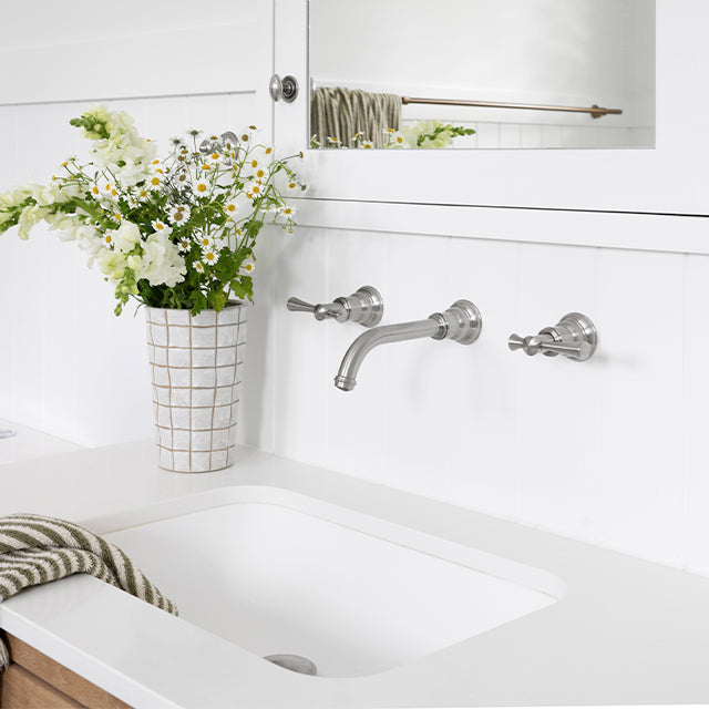 Phoenix Cromford chrome wall basin/bath tap set with spout, shown installed above a white vanity basin in a bathroom setting