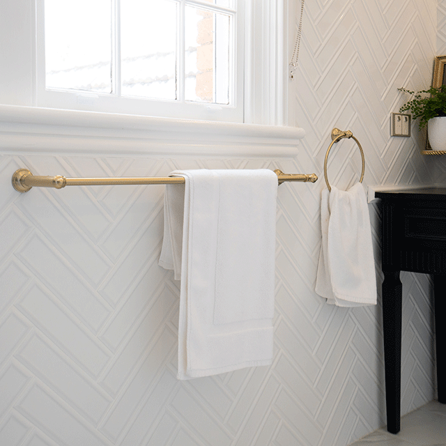 Phoenix Cromford single towel rail in brushed gold, mounted in a bathroom with white towels hung on it.