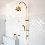 Phoenix Cromford twin shower in brushed gold, with overhead rose and handpiece on a wall rail in a tiled bathroom