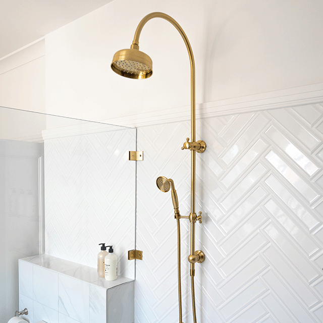 Phoenix Cromford twin shower in brushed gold, with overhead rose and handpiece on a wall rail in a tiled bathroom