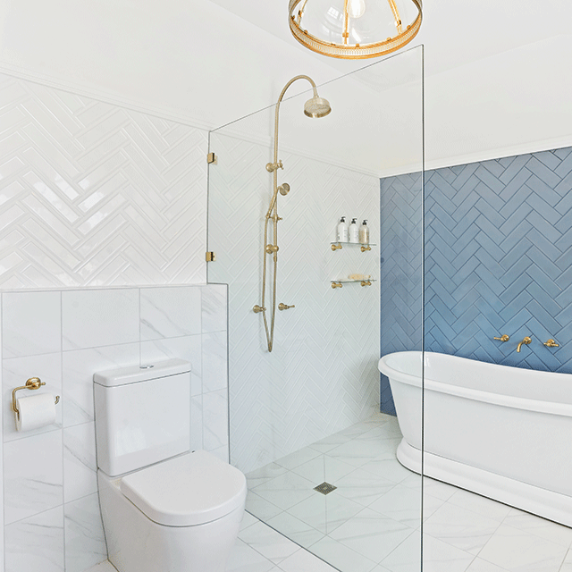Brushed gold Phoenix wall basin/bath outlet in a modern bathroom, with wall-mounted spout above a white freestanding bath and shower.