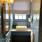 Phoenix Cromford glass bathroom shelf in brushed gold, wall-mounted beside basin in a blue tiled bathroom