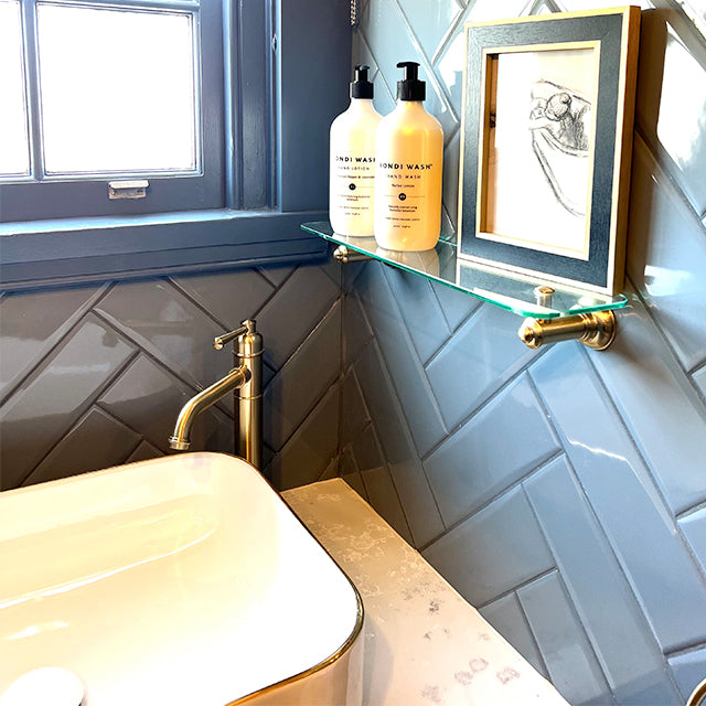 Phoenix Cromford glass bathroom shelf, 450mm, brushed gold bracket, styled in a modern bathroom with accessories