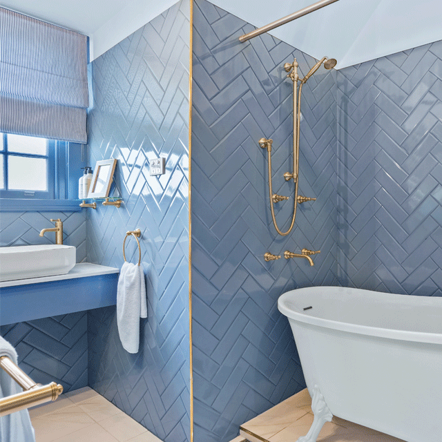 Phoenix Cromford brushed gold rail shower in a blue tiled bathroom, with matching shower rail and handpiece above a white bath