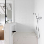 Phoenix Cromford chrome hand shower with hose and wall bracket, shown installed in a white tiled shower recess.