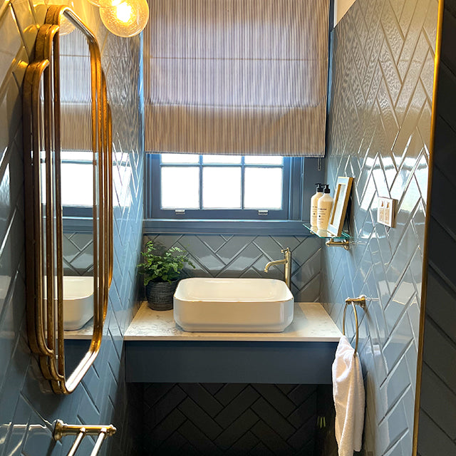 Phoenix Cromford brushed gold hand towel holder mounted on a blue bathroom wall beside a basin and mirror cabinet