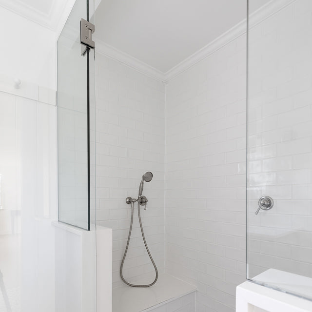 Phoenix Cromford brushed nickel wall shower mixer on a white tiled shower wall, with handheld shower fitting visible