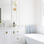 Phoenix Cromford chrome single towel rail mounted on white bathroom wall, holding a blue check towel beside a bathtub