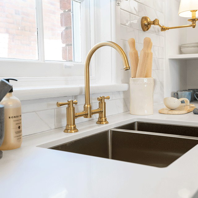 Phoenix Cromford exposed sink set in brushed gold, shown mounted above a kitchen sink with swivel spout and twin handles