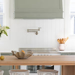 Phoenix Cromford wall mounted pot filler in brushed nickel, shown folded against a white kitchen splashback above a cooktop