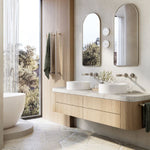 Phoenix heated triple towel rail in brushed nickel, mounted vertically beside a bathroom vanity with towels hung on it