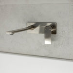 Phoenix Teel wall basin mixer set in brushed nickel, shown mounted on light stone tile with long spout and hot/cold handle