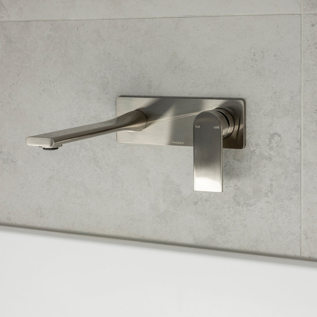 Phoenix Teel wall basin mixer set in brushed nickel, shown mounted on light stone tile with long spout and hot/cold handle