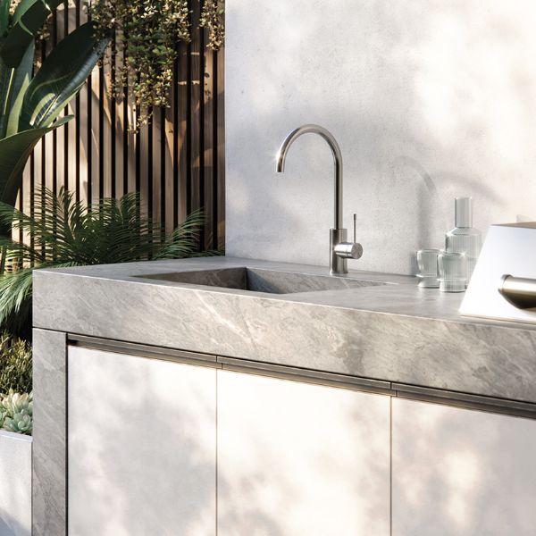 Phoenix Vivid Slimline stainless steel gooseneck sink mixer on a stone outdoor kitchen benchtop, side view with plants