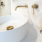 Phoenix Vivid Slimline brushed gold wall shower mixer with 60mm backplate, mounted beside a white bath and basin