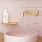 Phoenix Vivid Slimline wall basin mixer set in brushed gold, shown over a pink basin with wall-mounted spout and handle
