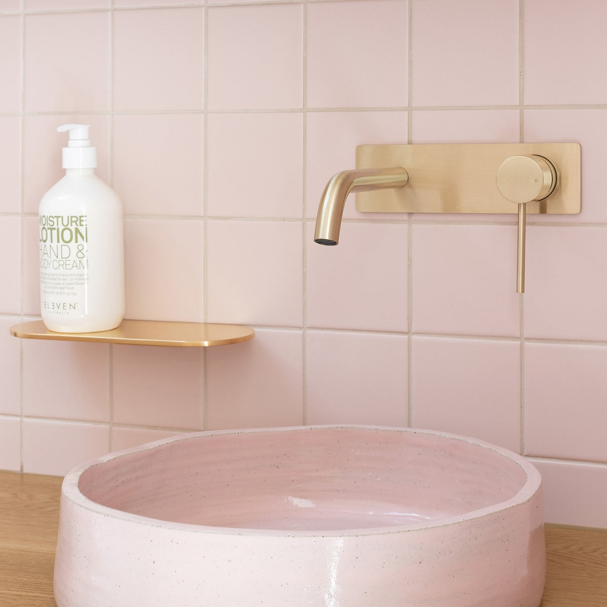 Phoenix Vivid Slimline wall basin mixer set in brushed gold, shown over a pink basin with wall-mounted spout and handle