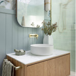 Phoenix Vivid Slimline wall basin mixer set in brushed gold, shown in a modern bathroom with round basin and mirror