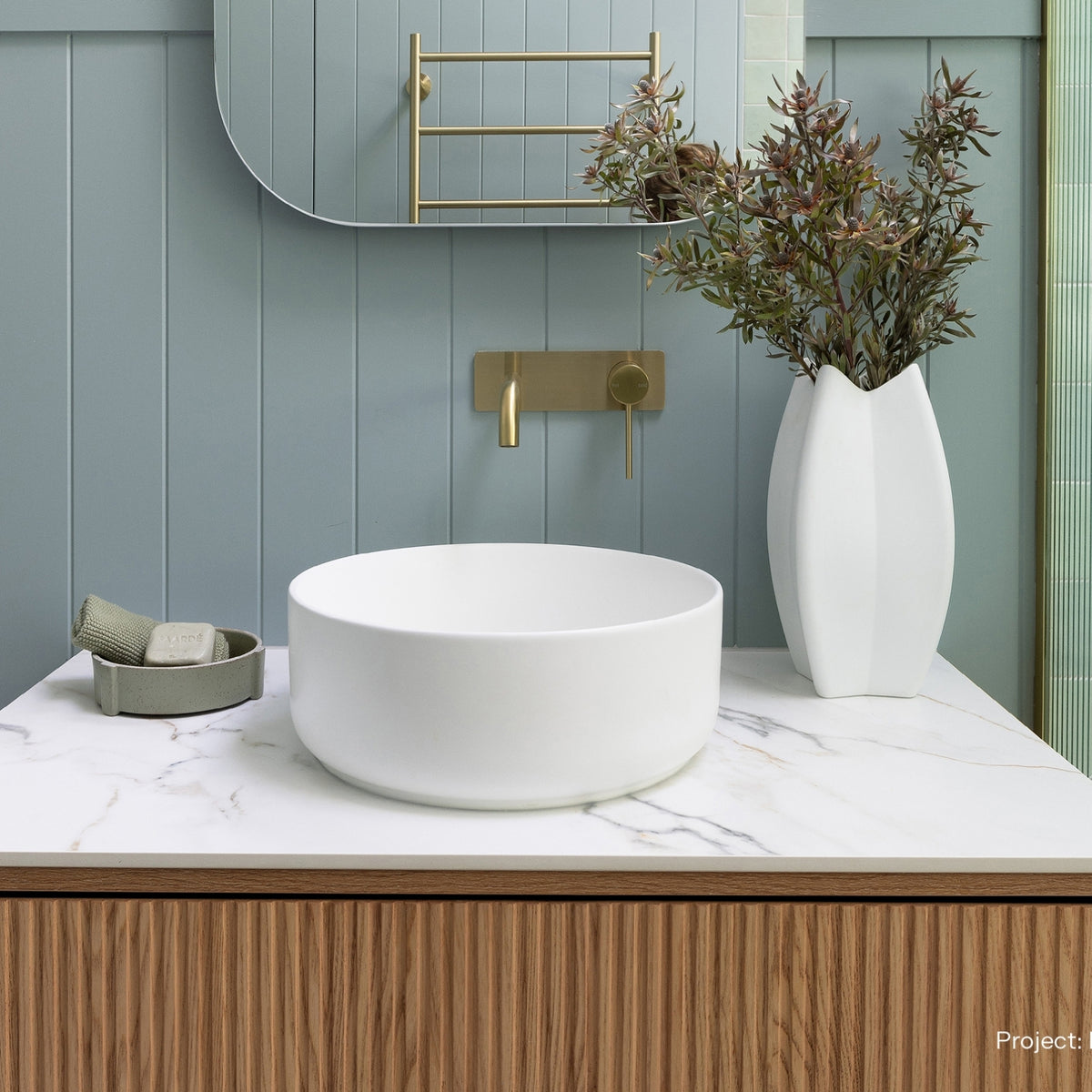 Phoenix Vivid Slimline wall basin mixer in brushed gold, shown above a white vessel basin in a modern bathroom vanity setting