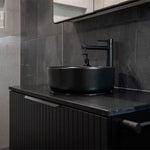 Phoenix Vivid Slimline vessel mixer in matte black, shown installed beside a black vessel basin in a modern bathroom vanity