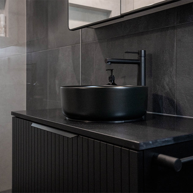 Phoenix Vivid Slimline vessel mixer in matte black, shown installed beside a black vessel basin in a modern bathroom vanity