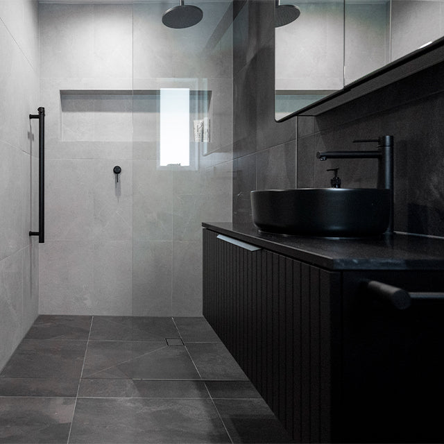 Phoenix Vivid Slimline vessel mixer in matte black beside a black above-counter basin in a modern bathroom vanity setting
