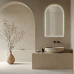 Radiant Ark frameless LED arch mirror in a warm bathroom setting above a vanity, with soft illuminated outline