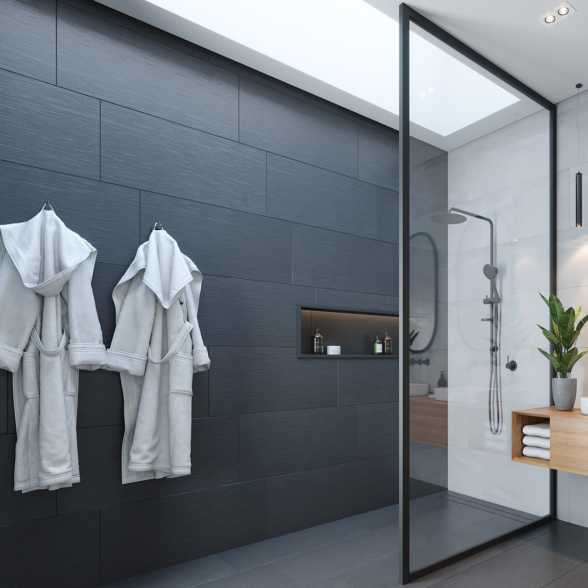 Modern bathroom with black wall hooks holding two grey bathrobes beside a glass shower and dark tiled wall