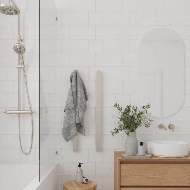 Thermogroup brushed nickel vertical single heated towel rail in a white bathroom with towel draped over it