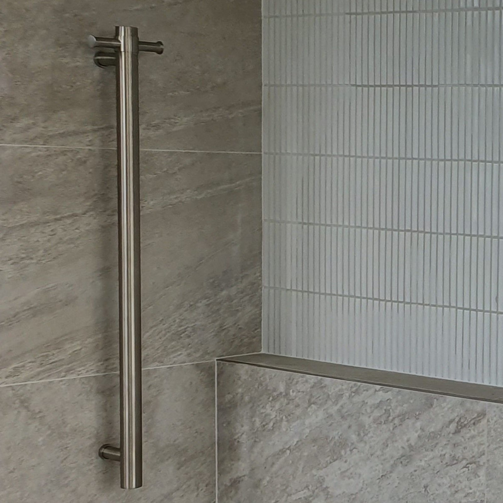 Thermogroup brushed nickel round vertical single bar heated towel rail installed on a tiled bathroom wall