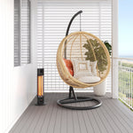 Thermogroup black freestanding outdoor heater beside a hanging egg chair on a covered patio