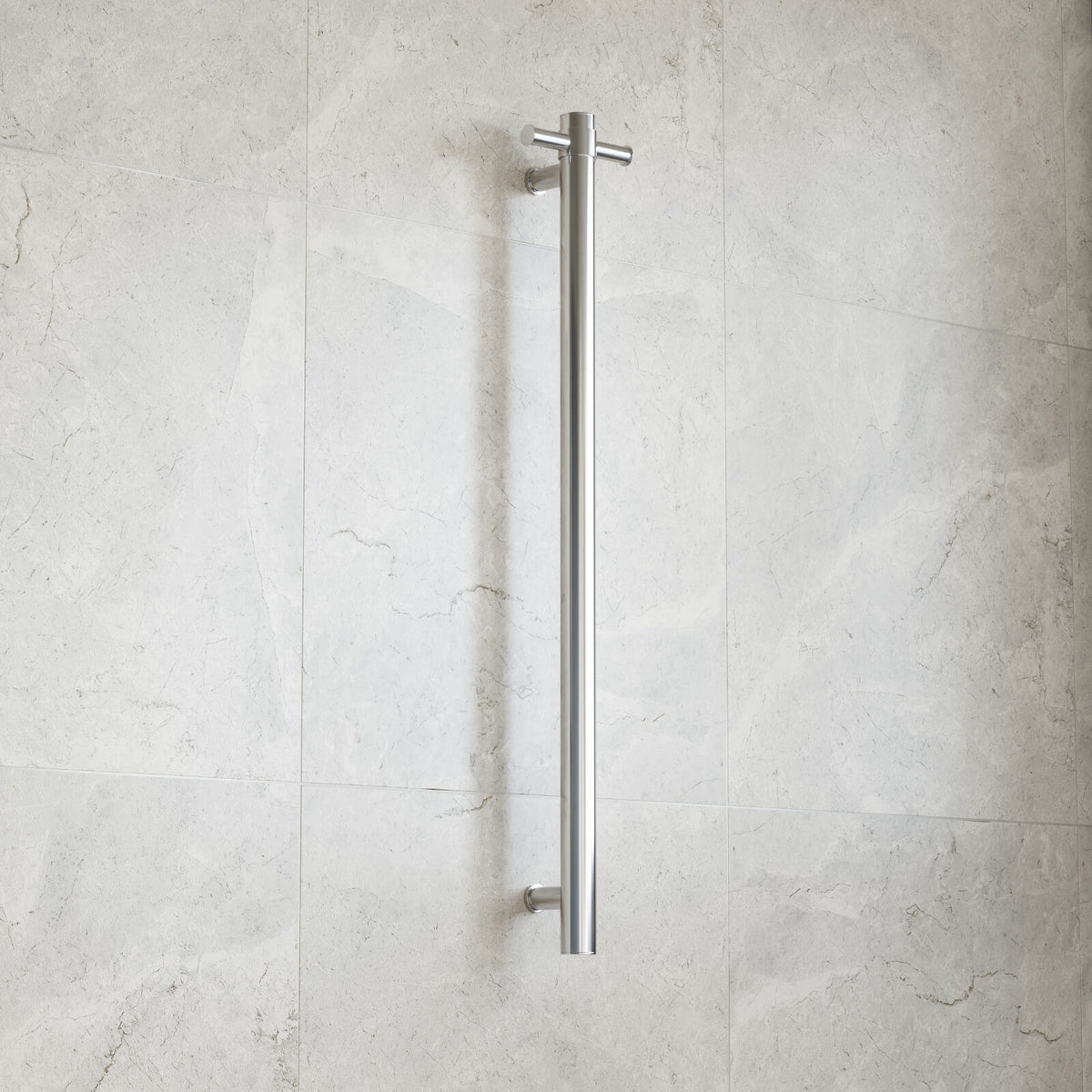 Thermogroup polished stainless steel heated towel rail, straight vertical single bar, wall mounted against light stone tiles
