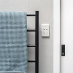 Thermogroup Thermorail black round towel ladder with 5 bars mounted beside a tiled shower wall with towel and control panel